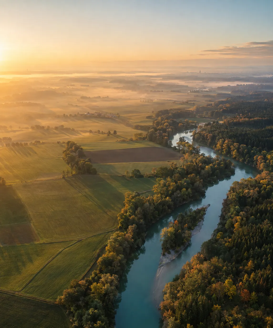 Luftaufnahme eines Flusses zwischen herbstlichen Wäldern und Feldern bei Sonnenaufgang